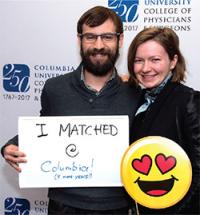 A man and woman smiling on Match Day, holding a sign that says "I matched @ Columbia!"